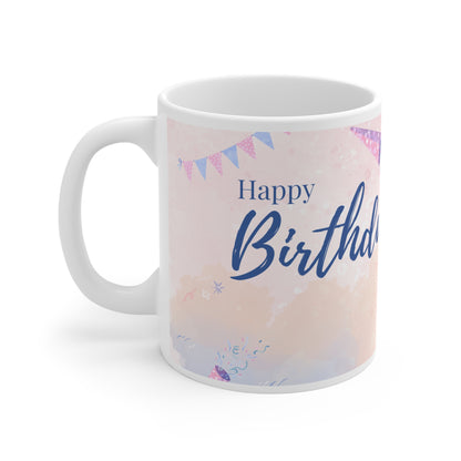 A white ceramic mug featuring a festive "Happy Birthday" design. The background is a soft pastel pink with watercolor-style splashes and subtle confetti accents. Above the "Happy Birthday" text in elegant blue script, there are colorful bunting flags in shades of pink, purple, and blue, adding a cheerful and celebratory touch to the mug's design.