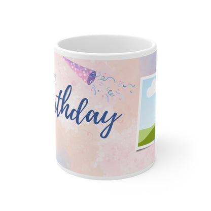A white ceramic mug featuring a festive "Happy Birthday" design. The background is a soft pastel pink with watercolor-style splashes and subtle confetti accents. Above the "Happy Birthday" text in elegant blue script, there are colorful bunting flags in shades of pink, purple, and blue, adding a cheerful and celebratory touch to the mug's design.